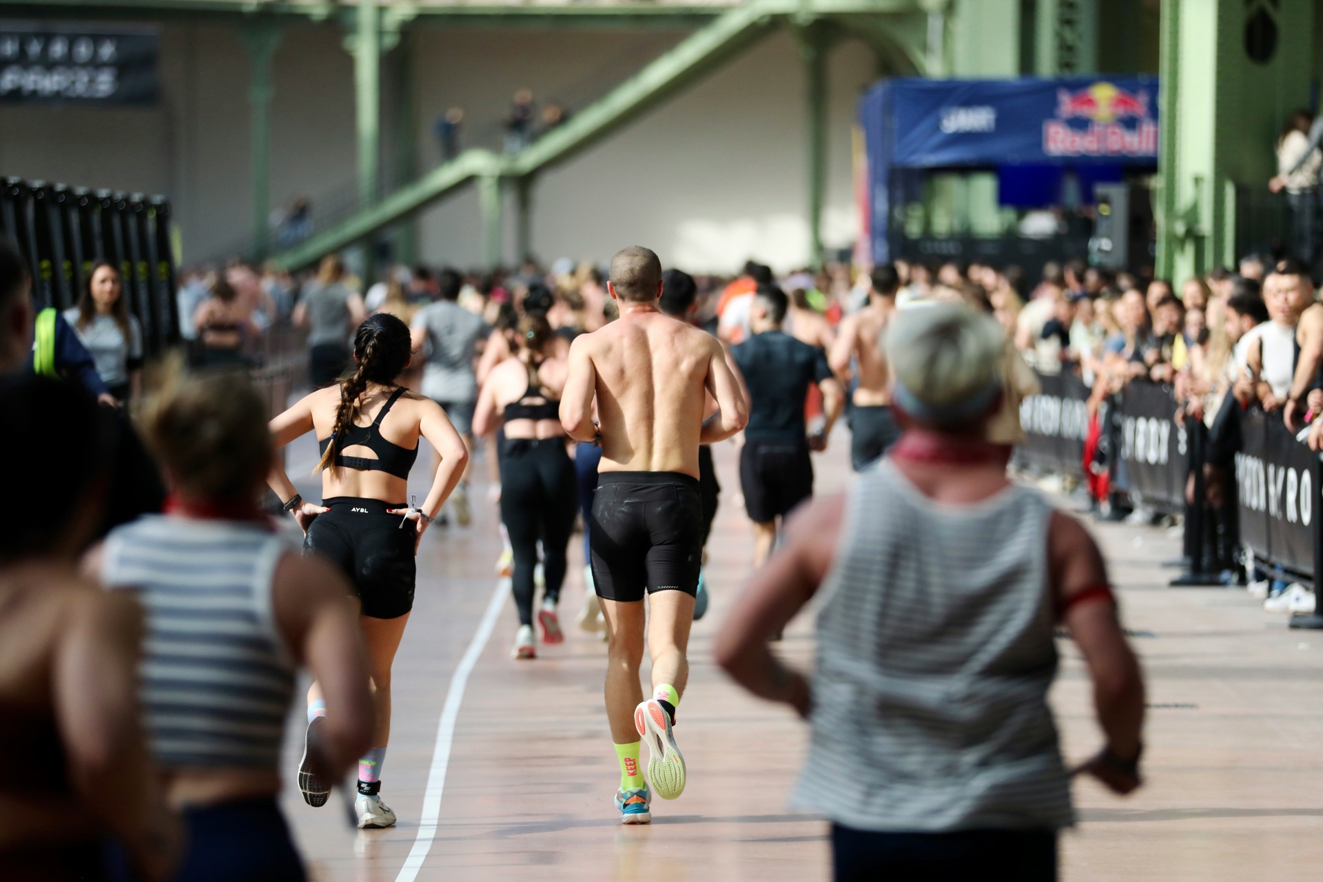 Runners mid-race on an indoor race floor, spectators watching from behind barriers.