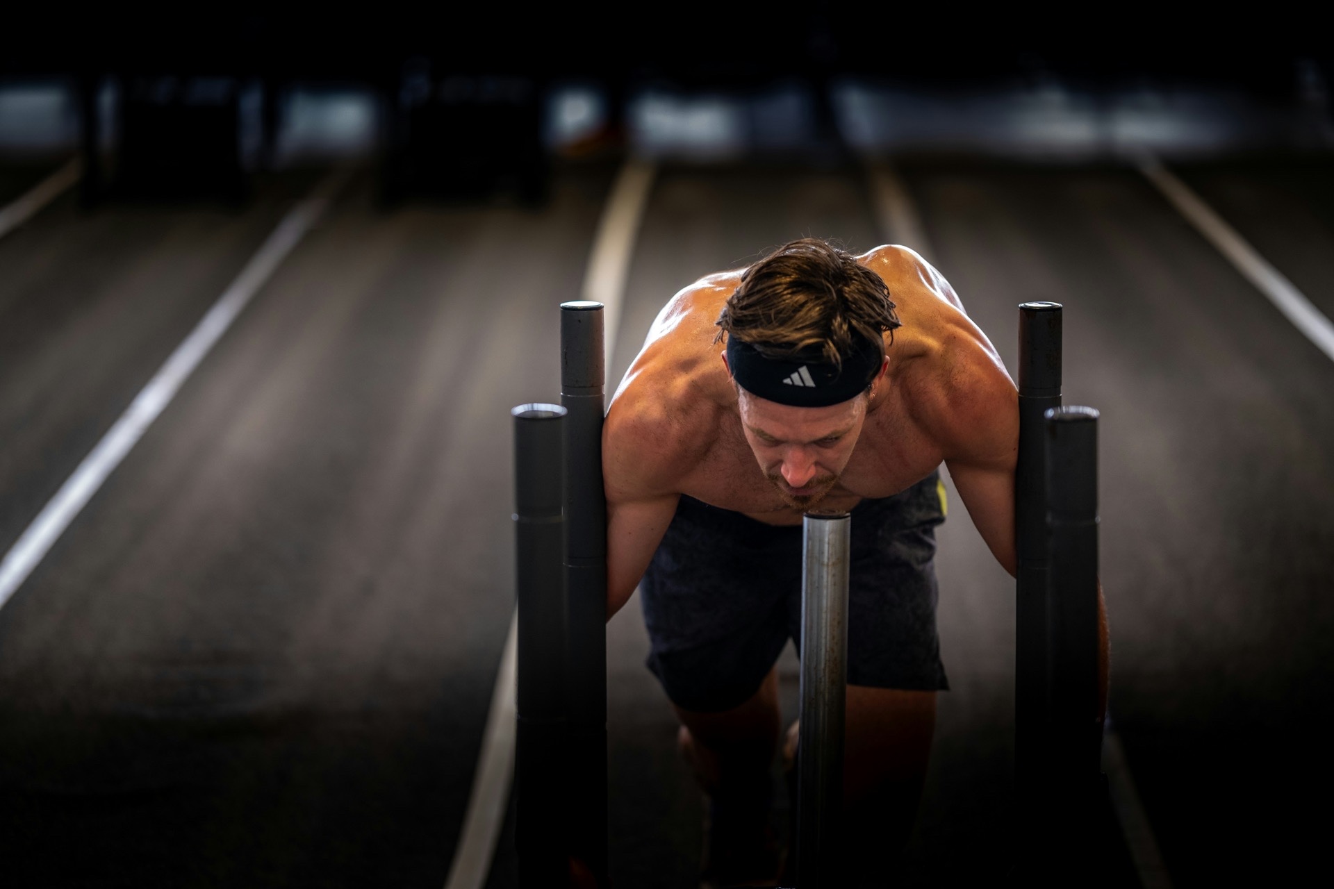 An athlete driving a weighted sled forward with his head down, arms locked on the uprights.