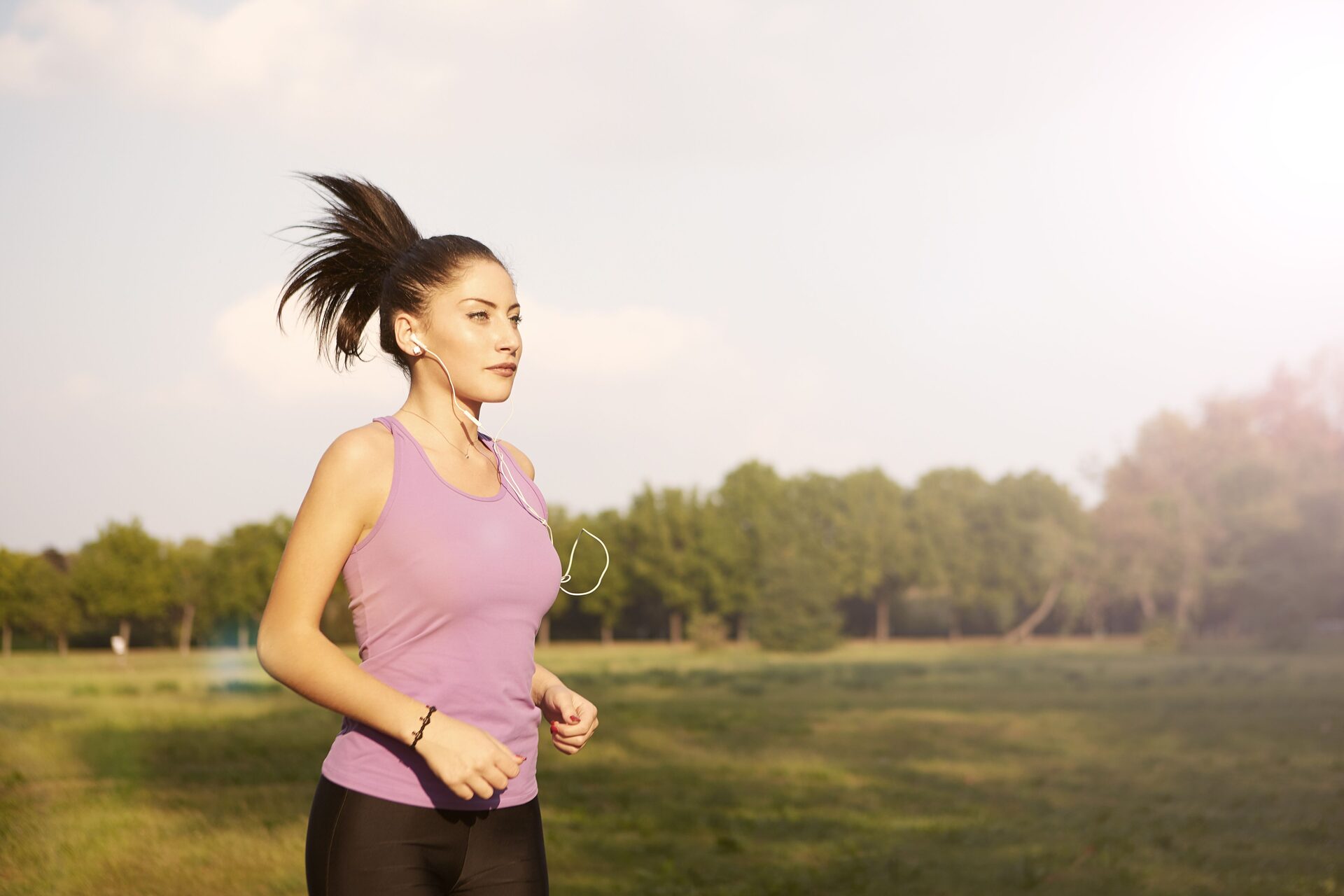 A runner on an easy run through a park at golden hour, earphones in, shot from the side.