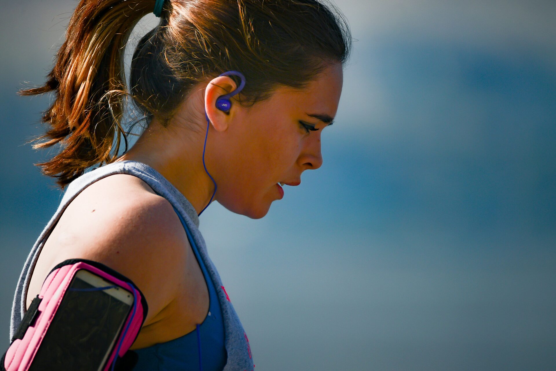 A runner catching her breath between reps, head down, earphone in, shot in close profile.