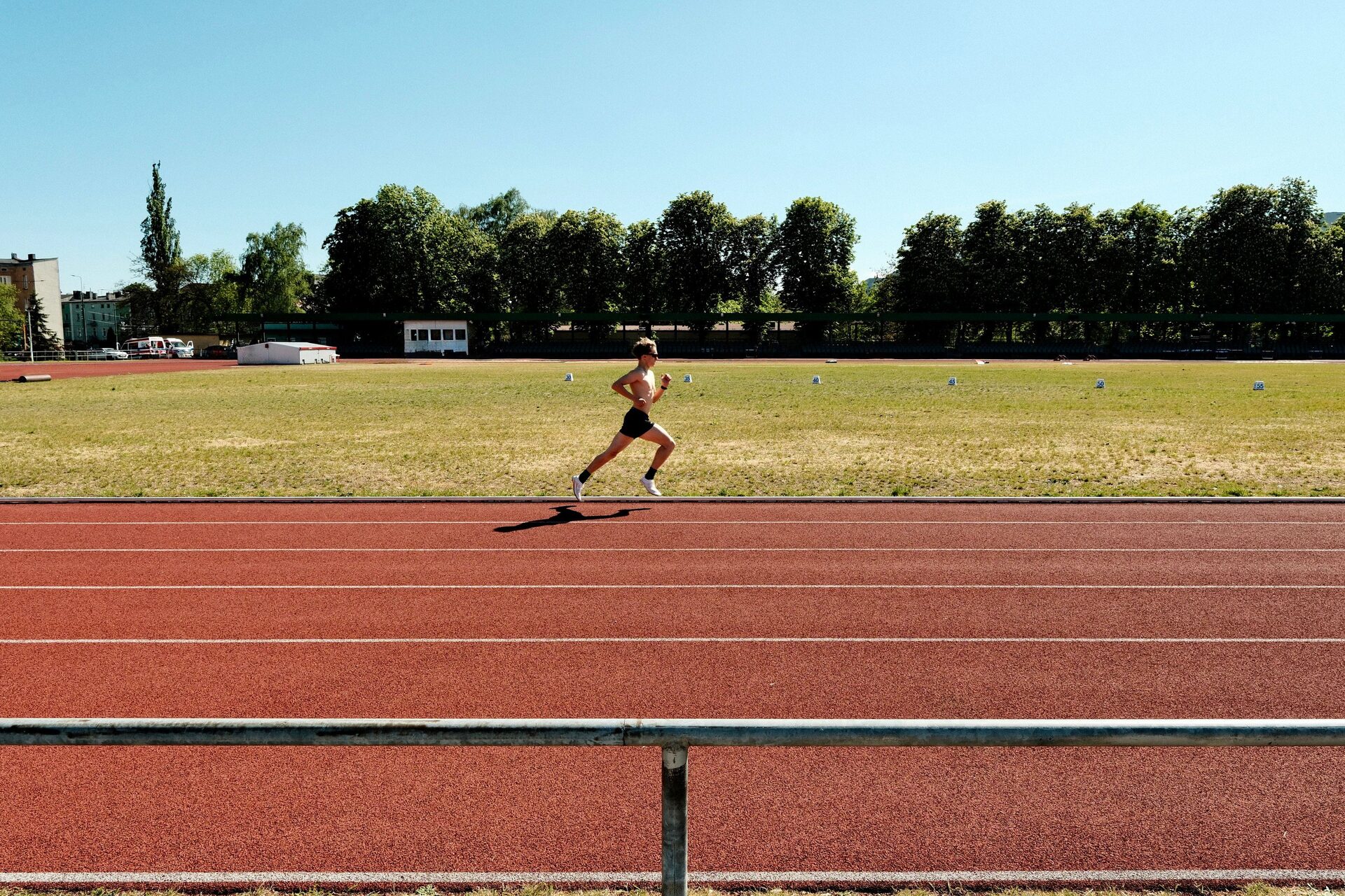 A lone runner mid-stride beside an empty track, lanes stretching across the frame.